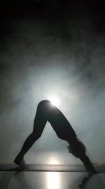 Siluet genç kadın karanlık spor salonunda buharla yoga yapıyor. Boşluğu kopyala