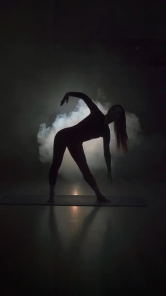若い女性のシルエットは 煙で暗いホールでヨガを練習しています ヨガの練習コンセプト — ストック動画