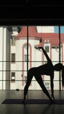 Sportif formda kadın silüeti bireysel hatha yogası, Vasisthasana eğitimi, pencerenin yanındaki spor salonunda bacak destek dengeleme pozisyonu. Sağlıklı yaşam tarzı kavramı