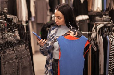 Modern kadın elbise mağazasında mesajlaşıyor ve sohbet ediyor. Güzel, genç, beyaz kadın alışverişçi. Boşluğu kopyala