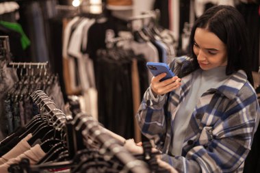 Güzel esmer kız elbise mağazasında akıllı telefonuyla barkodu tarıyor. Boşluğu kopyala