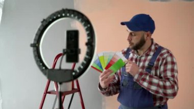 Erkek ressam vlogger yeni evi yenilerken canlı bir video yayınlıyor, palette renk örneklerini gösteriyor. Boşluğu kopyala