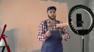 Erkek ressam vlogger yeni evi yenilerken canlı bir video yayınlıyor, telefonuyla video kaydediyor, kameraya paten fırçasını gösteriyor. Yenileme, inşaat ve blog konsepti