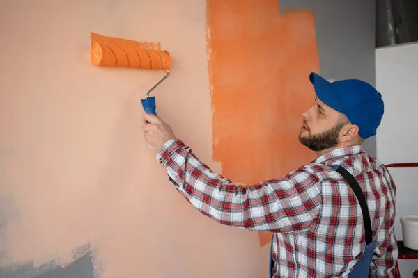 Bearded man painter painting a wall orange with a paint roller. Place for text. Copy space