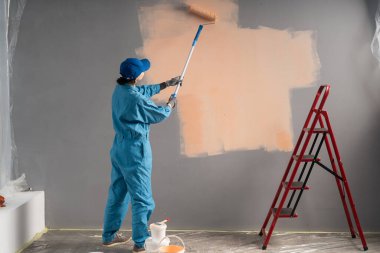 Şapkalı ya da boyacı duvarları uzun boyalı silindirle boyuyor. iş, inşaat, yenileme ve insan konsepti