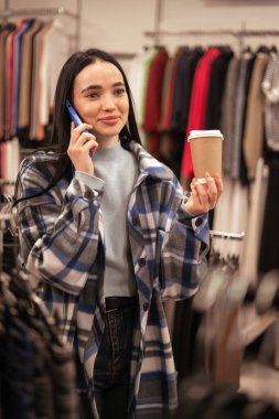 Bir elbise mağazasında bir müşteri bir arkadaşını arıyor ve elbise reyonlarında kahve içiyor. Bir kadın hafta sonları kıyafet seçer. Satış, moda ve alışveriş konsepti