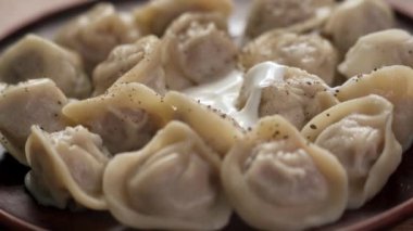 Ekşi kremayla servis edilen etle doldurulmuş buğulanmış hamur köfteleri. Ukrayna mutfağı yemekleri. Yakın plan.