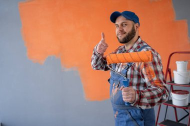 Sakallı bir ressam, turuncu duvarı boyayarak odada dikiliyor. Pankart. Boşluğu kopyala