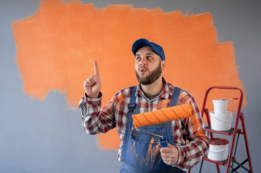 Boya silindirli ressam portresi parmak kaldırma ve şok olmuş yüz ifadesi sergiliyor, arka planda duruyor. Metin için boşluk.
