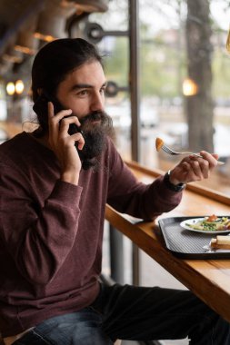 Hipster bir kafede ya da fast food restoranında öğle yemeği yiyor, tepside yemek yiyor, sağlıklı besleniyor, diyet yapıyor, öğle arasında telefonla arıyor. Boşluğu kopyala