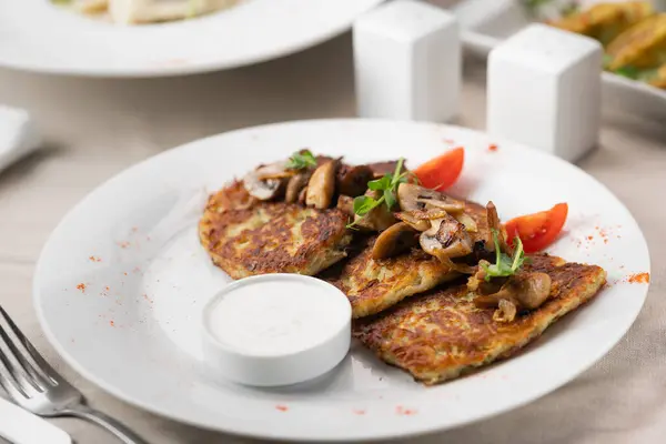 Potato pancakes with mushrooms. Potatoes pancakes on white plate with sour cream. Copy space for text.