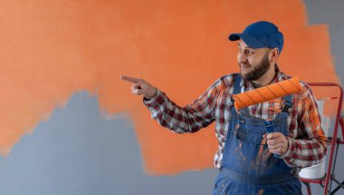 Ressam ya da dekoratör yüzünde bir gülümseme olan silindir tutan, kameraya el ile işaret eden bir adam. Boşluğu kopyala