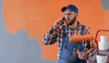 Boyacı cep telefonundan arıyor, elinde boya silindiri tutuyor, evini yeniliyor. Boşluğu kopyala