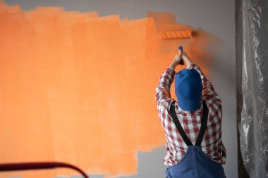 Boyacı duvarları boya rulosu ve turuncu renklerle boyuyor. Büyük bir boşluk. Boşluğu kopyala