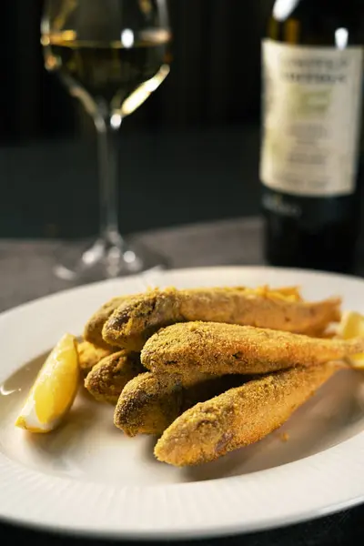 Fried red mullet serving on white plate. Fish and wine in restaurant. Copy space