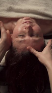 Sağlık merkezinde kafa masajı yapan bir masör. Olgun bir kadının kaplıcada yüz masajı yaptırdığı yakın plan fotoğraf. Yaşlanma karşıtı tedavi kavramı.