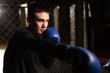 Boksör bir boks stüdyosunda yumruk pratiği yapıyor. Bir boks kafesinin içine yumruk atan genç adam, yakın plan. Boşluğu kopyala