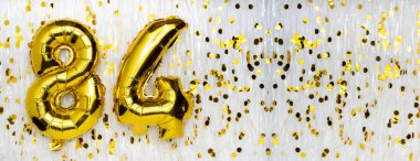Altın folyo balon numarası, seksen dört. 84 yazısıyla birlikte doğum günü tebrik kartı. Yıldönümü kutlaması. Pankart. Altın rakamlı, beyaz arkaplan. Sayısal rakam. Boşluğu kopyala
