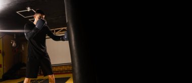 Spor kavramı. Güçlü atletik genç adam kendini savunma yumruklarını boks eldivenleriyle eğitiyor. Pankart. Boşluğu kopyala