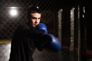 Boksör bir boks stüdyosunda yumruk pratiği yapıyor. Bir boks kafesinin içine yumruk atan genç adam, yakın plan. Boşluğu kopyala