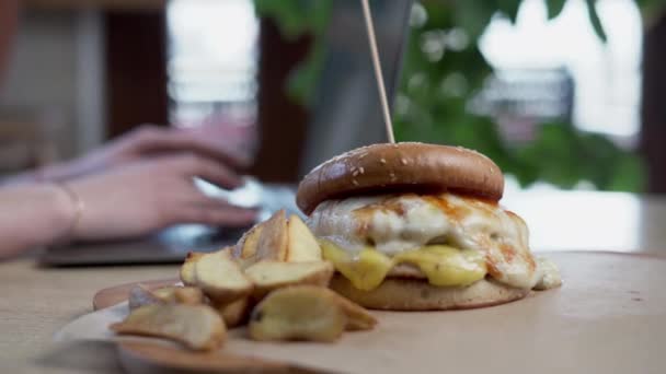 おいしいハンバーガーやチーズバーガーは リモートでラップトップ 選択的なフォーカスで作業するクライアントフリーランサーにカフェでフライドポテトを提供しました クローズアップ — ストック動画