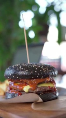Fast food kafede siyah çöreğin içinde lezzetli sıcak burgerin yakın plan çekimi. Makro manzara. Dikey video