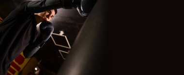 Eldivenli boksör, kum torbasında kum torbasına çarpar, sıkı antrenman yapar. Spor konsepti. kopyalama alanı. Pankart. düşük açı