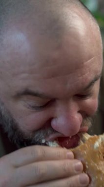 Sakallı adam kafede etli büyük bir burger yiyor, yakın plan. Boşluğu kopyala