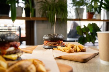 İki lezzetli siyah burger ve patates kızartması bir restoranda ya da kafede ahşap tahtalarda servis ediliyor. Boşluğu kopyala