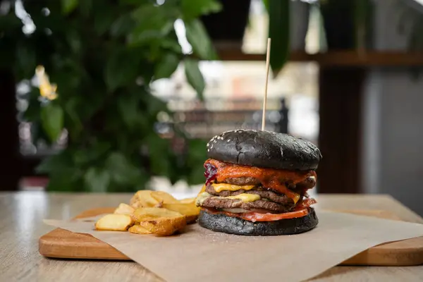 Black double burger served with fries on a wooden board on a table in a cafe. Fast food concept. Copy space