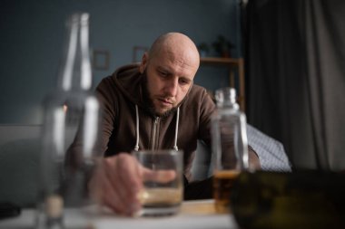 Sarhoş adam ya da erkek alkolik evde viski içip bir sürü şişenin arasında oturuyor. Alkolizm, alkol bağımlılığı ve insanlar konsepti