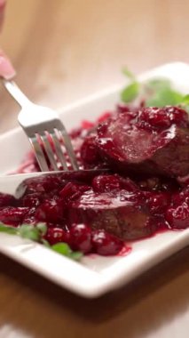 Beyaz tabakta servis edilen vişne soslu geleneksel yaban tavşanı filetosu yiyen kadın ellerinin yakın çekimi. Restoran menüsü. Dikey video