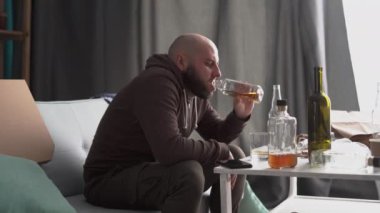 Ağır depresyonda olan sakallı bir adam evde alkol içiyor. Taciz ve alkolizm konsepti. Yan görünüm