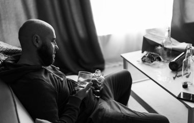 Üzgün, alkolik, alkolik, evde tek başına viski içen alkolik, alkolik, alkol bağımlılığı sorunu olan bağımlı bir adam. Alkolizm konsepti. Siyah beyaz fotoğraf