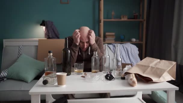 酔っ払った男は 自宅でソファーに座ってアルコールを飲んでいる 疲れた男性は ボトルでテーブルの前に頭を抱えている問題について考えます コピースペース — ストック動画