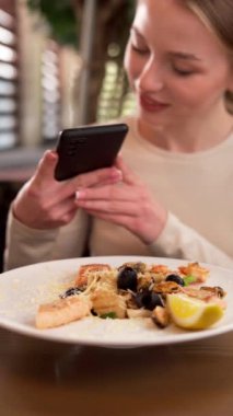Genç kız fotoğraf çekerken mobil kamerada deniz ürünleri ve Akdeniz salatasının akıllı telefonuyla fotoğraf çekiyor. Yemek fotoğrafçısı ve blog konsepti
