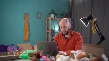 Diz üstü bilgisayarında yemek ve çöplerle oturan pasaklı sakallı bir adam. Boşluğu kopyala