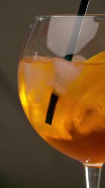 Gri arka planda bir bardak Aperol Spritz kokteyli. Aperol Spritz ile kokteyl pipetini karıştırıyorum. Dikey video