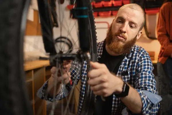 Bearded redhead male mechanic repairing a bicycle in a garage or workshop. Close-up