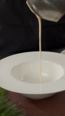Şef, restoranda beyaz tabağa kremalı çorba dolduruyor. Yemek pişirme konsepti. Dikey video