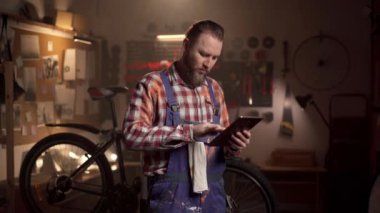 Sakallı milenyum adamı bisiklet tamirhanesinde çalışıyor ve dijital bloknotlara bakıyor. Boşluğu kopyala