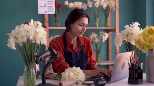 美しいヒスパニック系女性起業家は ラップトップにタイピングする花屋で働いています 花屋のエプロンの女性 フローリストのコンセプト — ストック動画