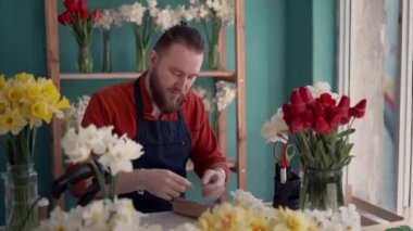 İş yerinde çiçek buketi yapan çekici bir çiçekçinin portresi. Çiçekçide oturan konsantre sakallı erkek. Boşluğu kopyala