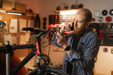 Bisiklet tamirhanesinde ya da garajda çalışan tamirci, cep telefonundan arayan, özel aletlerle bisiklet tamir eden teknisyen. Boşluğu kopyala