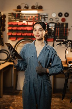 Kırık bir bisikleti tamir eden genç bir kadın atölyede ya da garajda çalışan teknolojiyi kullanır. Dijital tabletli bir kadın bisikletçi. Boşluğu kopyala