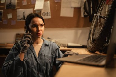 Dizüstü bilgisayarına bakarken atölyesinde genç bir kadın. İş yerinde dizüstü bilgisayarı ve cep telefonu olan bir bisikletçi. Boşluğu kopyala