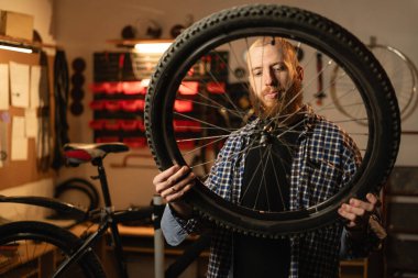 Sakallı adam atölyesinde ya da garajında tek başına duruyor ve bisiklet tekerleğini tamir ediyor. Boşluğu kopyala