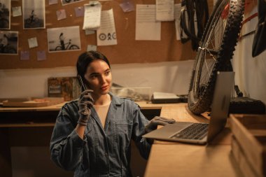 Dizüstü bilgisayarına bakarken atölyesinde genç bir kadın. İş yerinde dizüstü bilgisayarı ve cep telefonu olan bir bisikletçi. Boşluğu kopyala