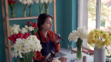 Çiçekçi kadın, küçük işletme sahibi çiçekçi dükkanında oturan akıllı telefonu kullanarak sesli mesaj kaydediyor.