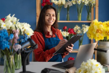 Gülümseyen çiçekçinin portresi küçük bir çiçekçi dükkanı sahibi. Mağazasının siparişlerini almak için dizüstü bilgisayarını ve panosunu kullanan bir kadın. Boşluğu kopyala